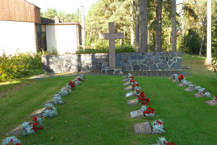 minnesmärket över stupade: ett stort kors i granit med en mur bakom, liggande gravstenar i rad